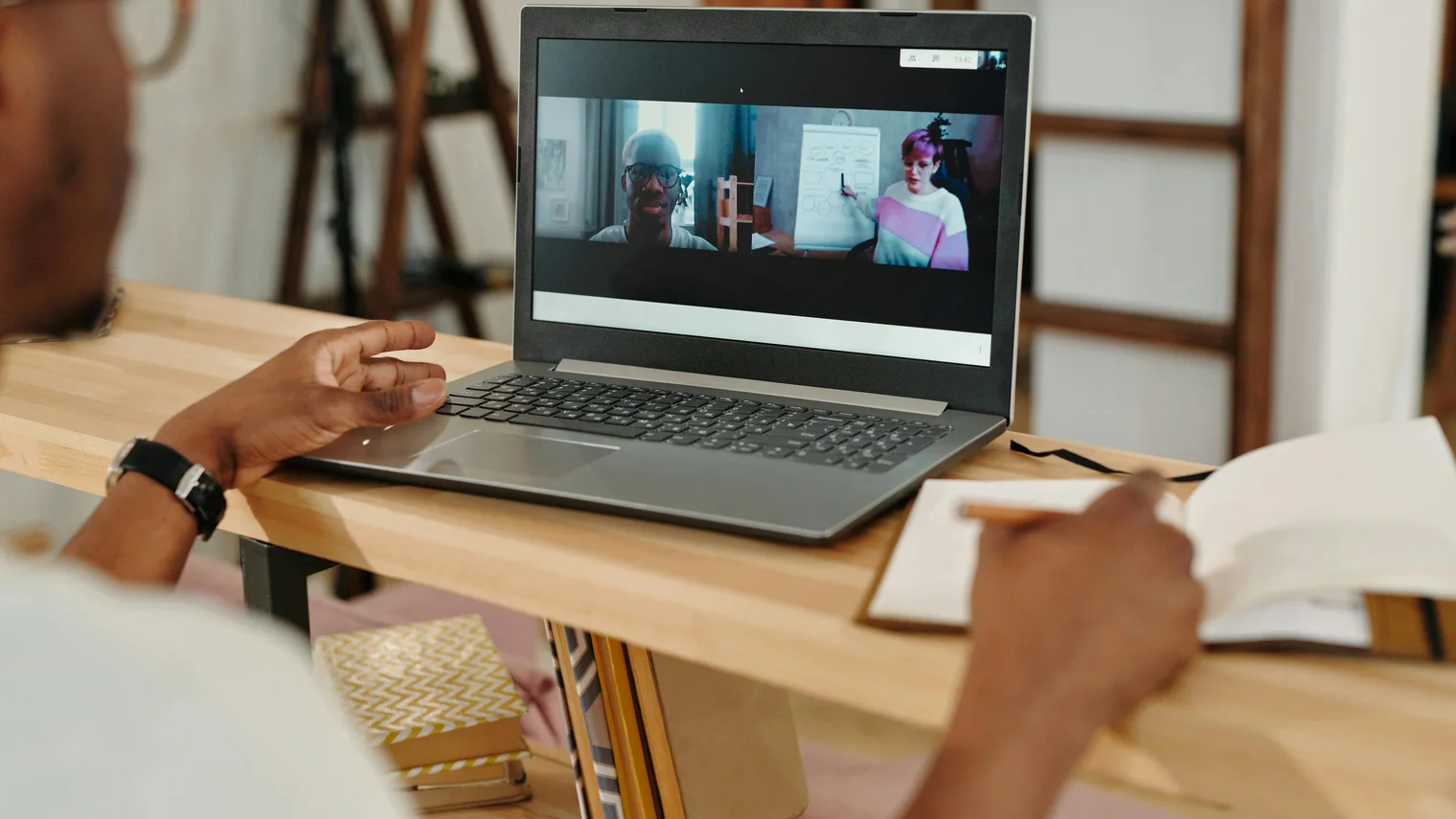 Candidate taking notes during a video interview call with a laptop screen and notebook visible