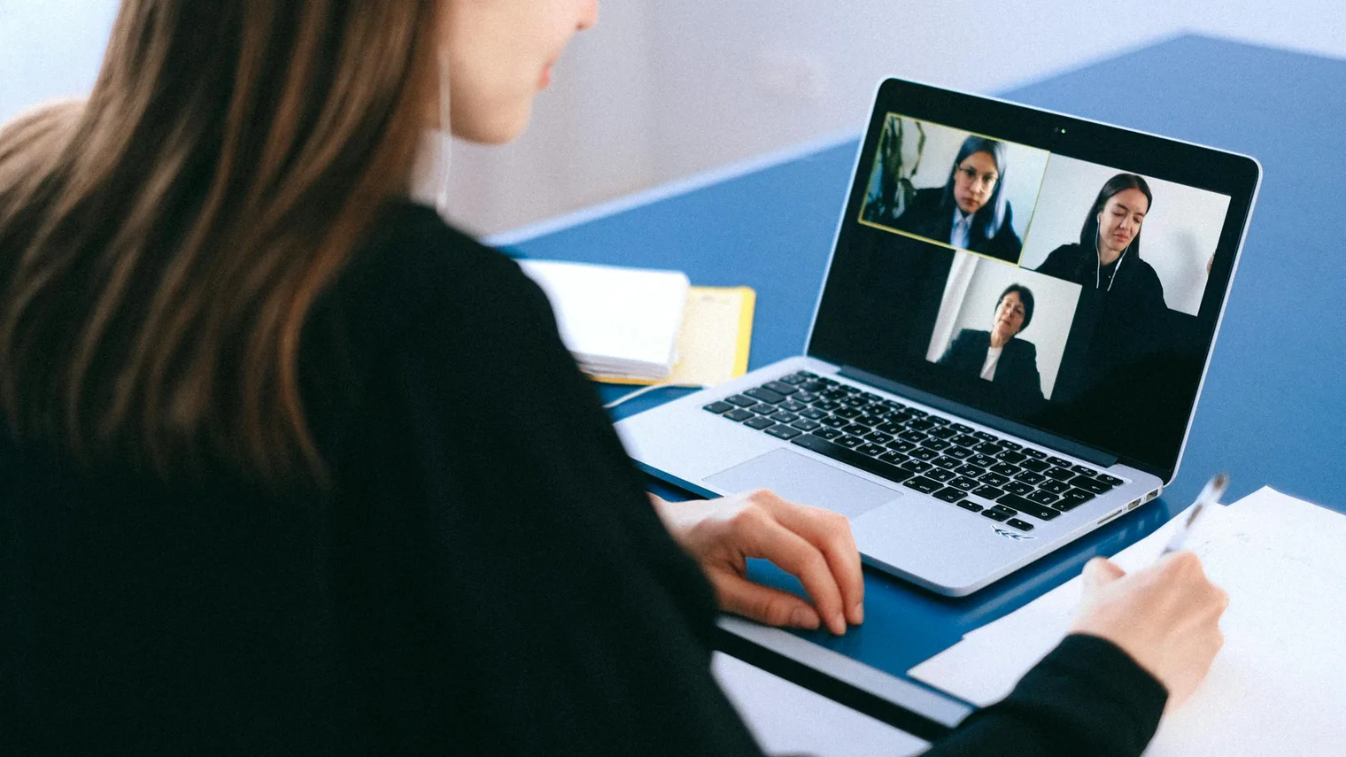 Candidate taking notes beside a laptop video interview with short prompts visible on paper